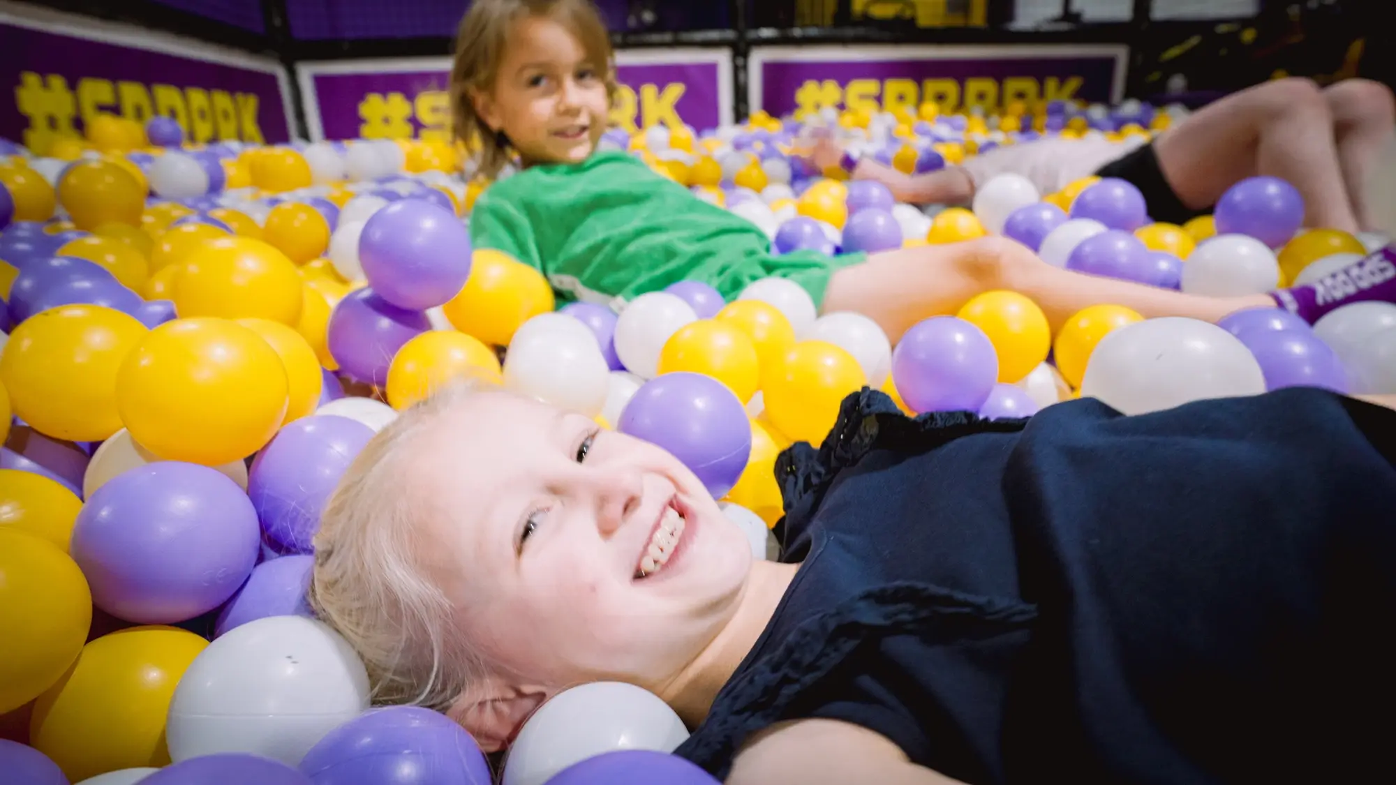 Two children playing in a ball pit in an indoor playground